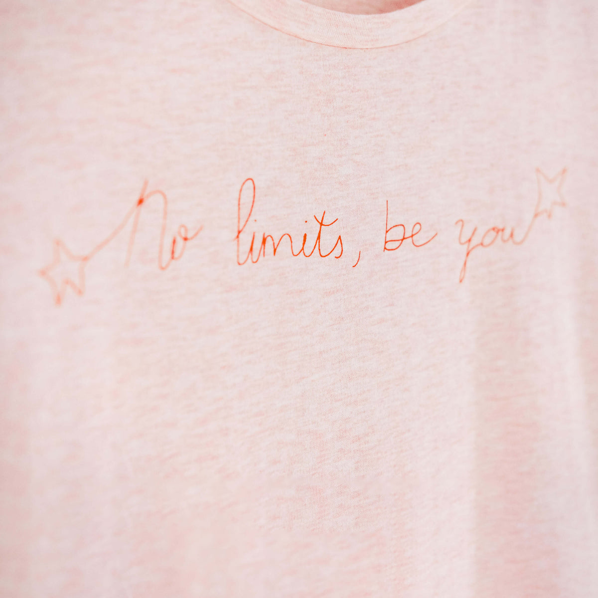 Detalle de texto estampado en color naranja. Camiseta rosa de mujer, de algodón orgánico y estampada a mano con tintas ecológicas.