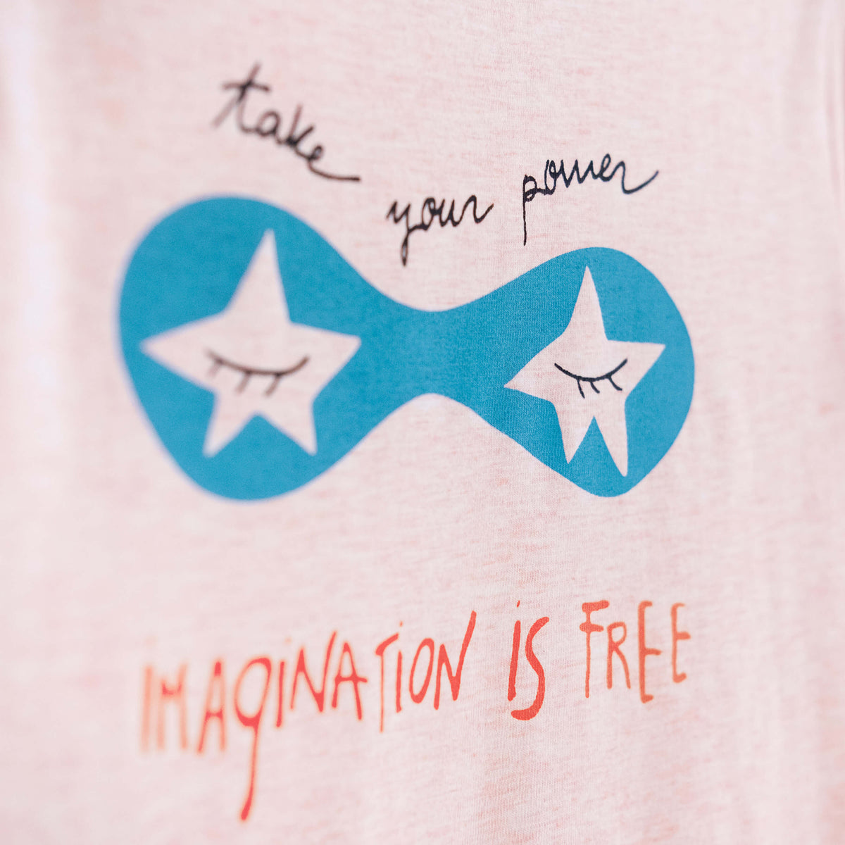 Detalle de texto serigrafía en color negro, azul y naranja. Camiseta rosa de algodón orgánico para niños, estampado a mano con tintas ecológicas. Modelo unisex.